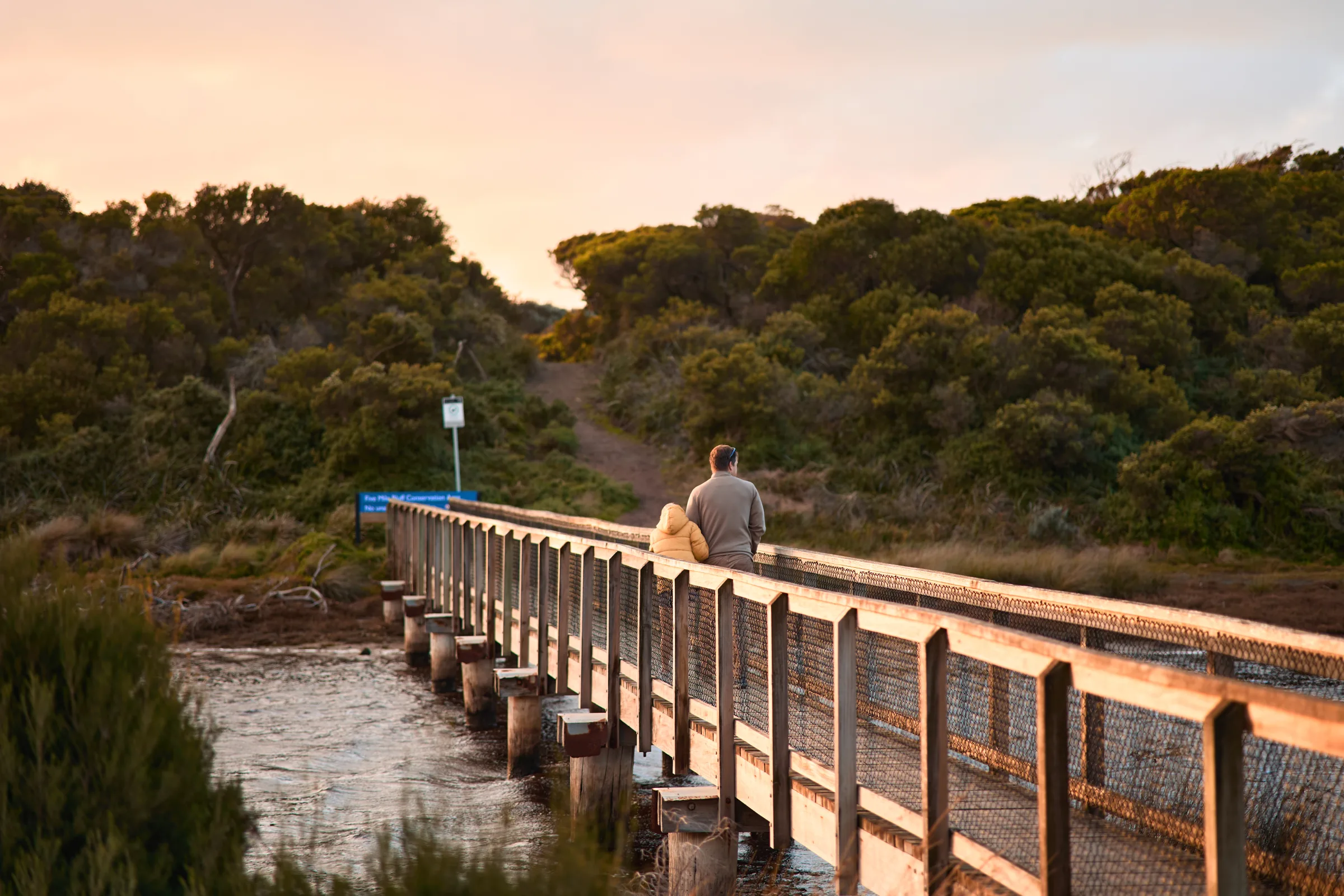 A man crossing the boardwalk bridge at sunset
